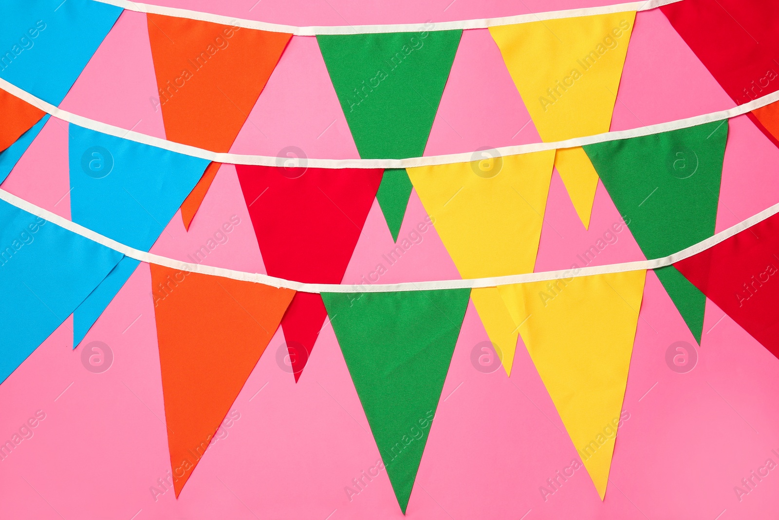 Photo of Buntings with colorful triangular flags on pink background. Festive decor