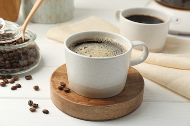 Aromatic coffee in cup and beans on white wooden table