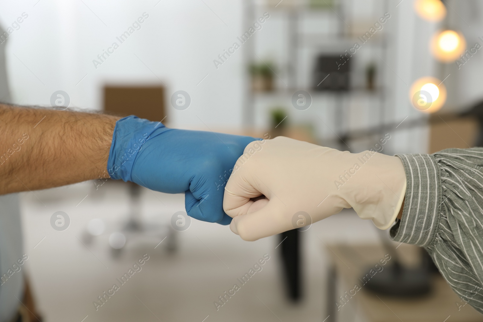 Photo of People greeting each other by bumping fists instead of handshake in office, closeup