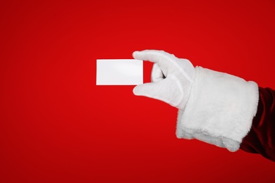 Photo of Santa Claus holding blank card on red background, closeup of hand. Space for text