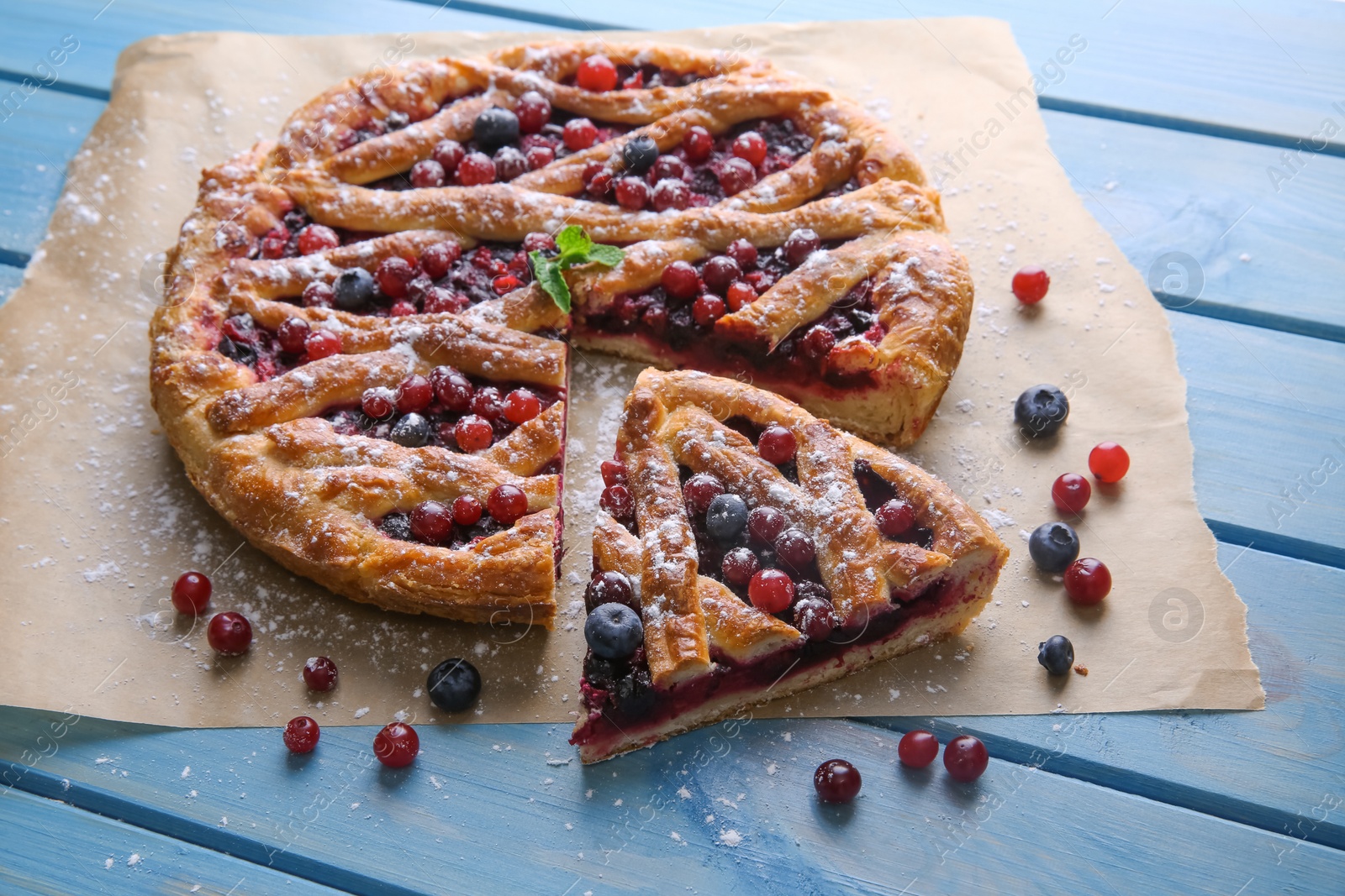 Photo of Delicious cut currant pie and fresh berries on blue wooden table