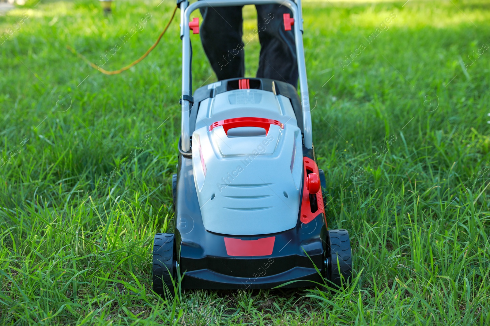 Photo of Man cutting grass with lawn mower in garden, closeup