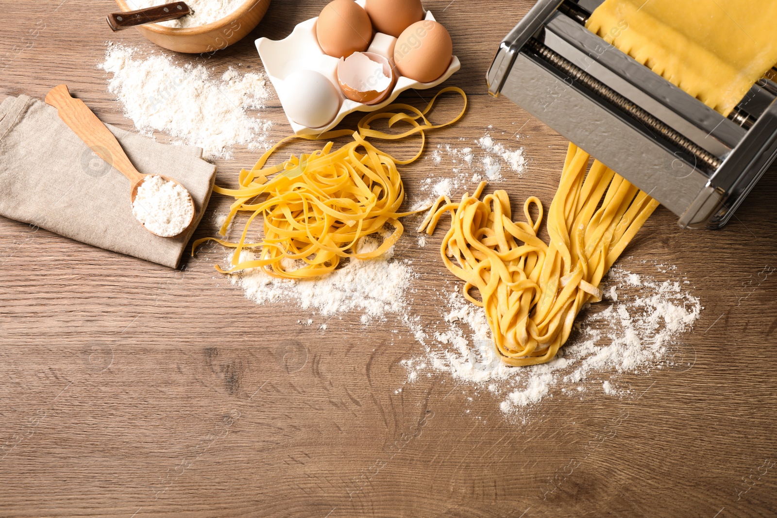 Photo of Pasta maker machine with dough and products on wooden table, above view. Space for text