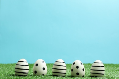 Photo of Line of traditional Easter eggs decorated with black paint on green lawn against color background, space for text