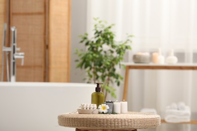 Photo of Spa products, burning candles and plumeria flower on wicker table in bathroom. Space for text