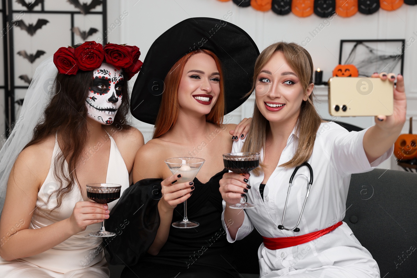 Photo of Group of women in scary costumes with cocktails taking selfie at Halloween party indoors