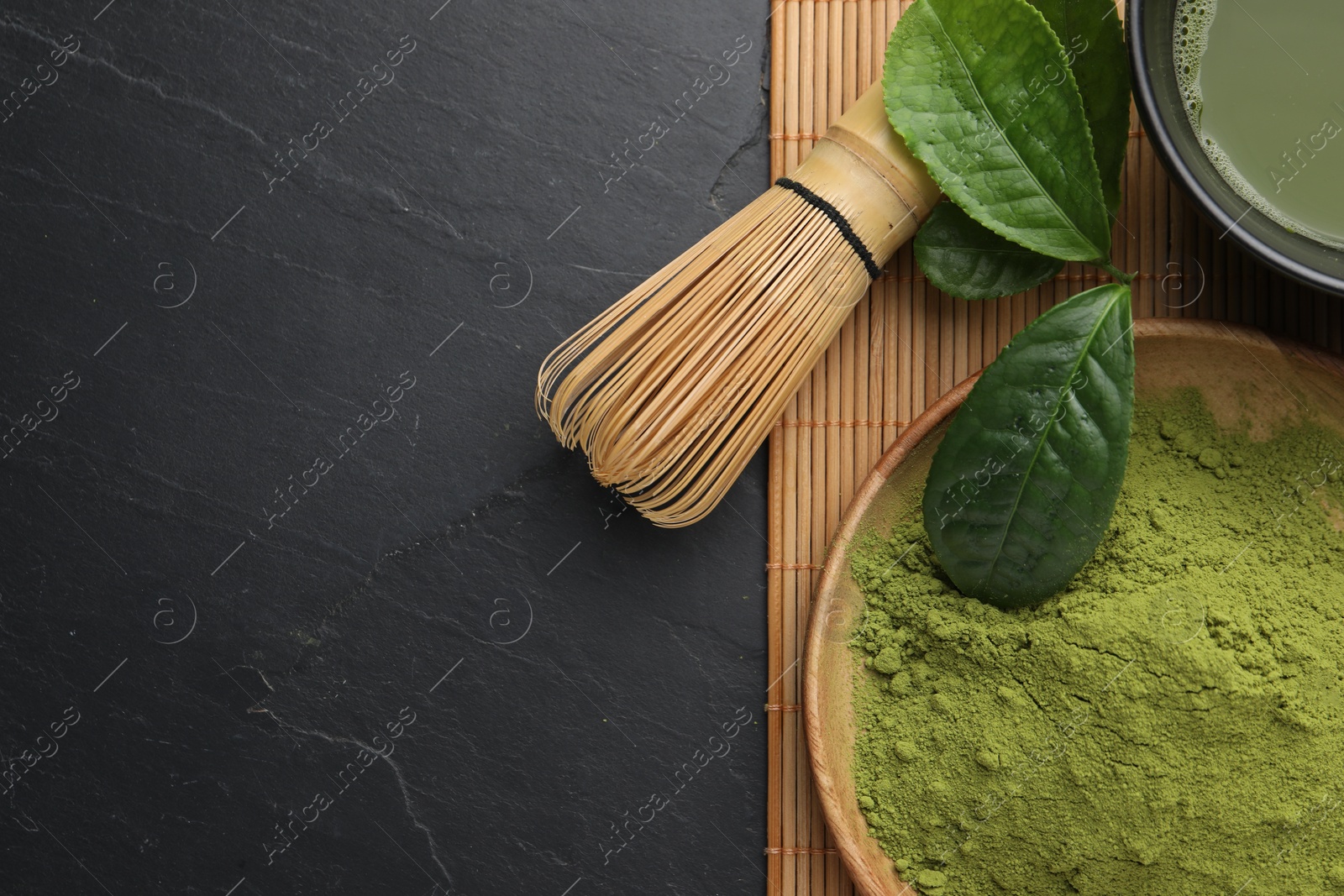 Photo of Green matcha powder, bamboo whisk and leaves on black table, flat lay. Space for text