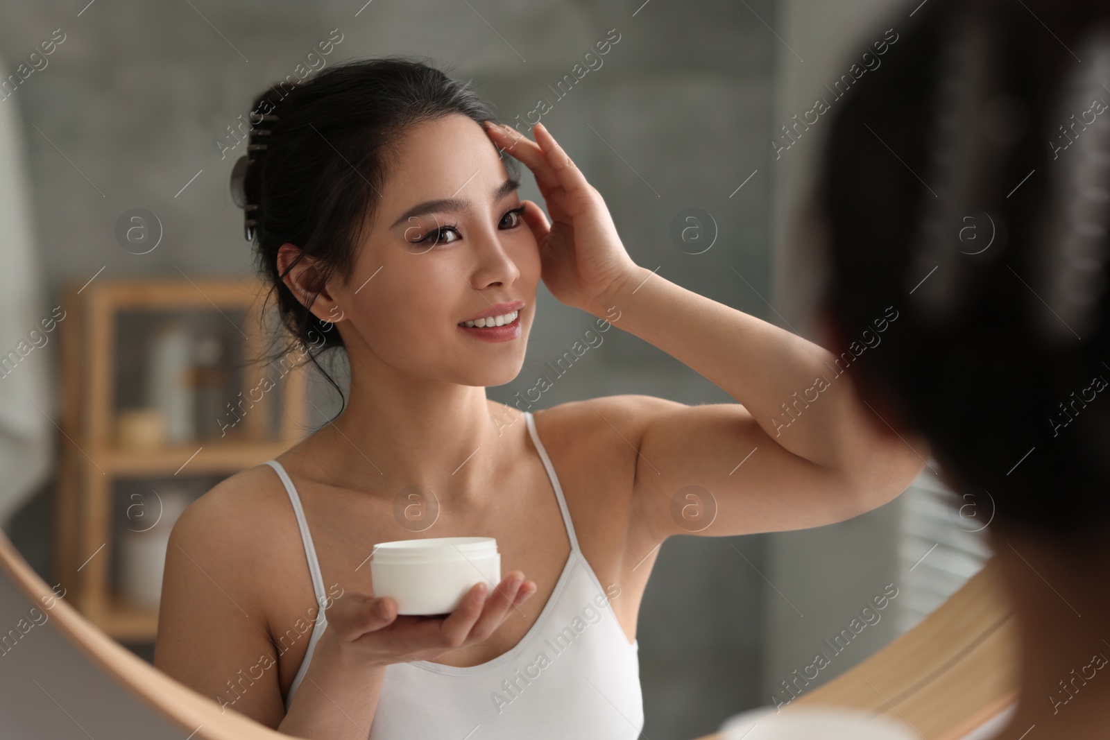 Photo of Happy woman applying face cream near mirror at home