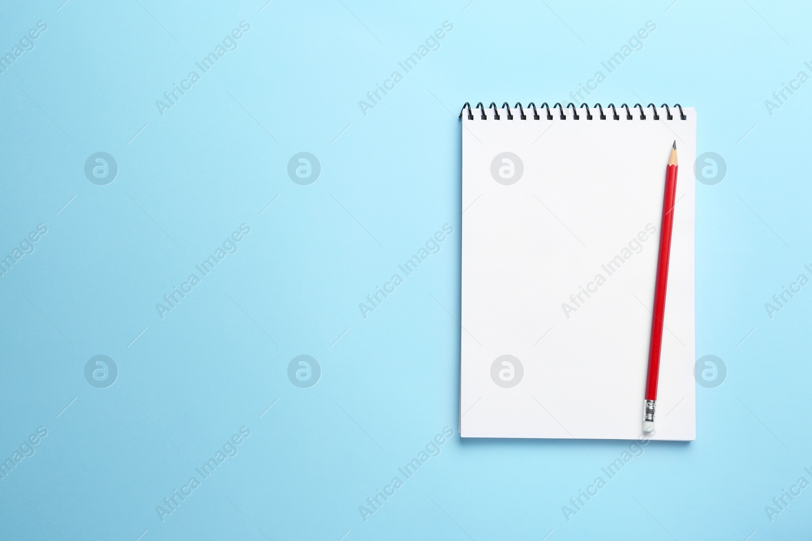 Photo of Notebook and pencil on light blue background, top view. Space for text