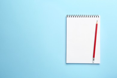 Photo of Notebook and pencil on light blue background, top view. Space for text