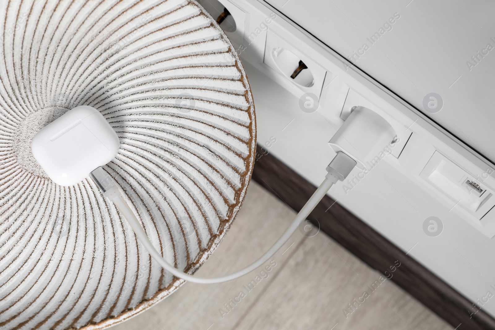 Photo of Modern wireless earphones charging from electric socket indoors, above view