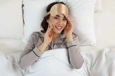 Photo of Beautiful young woman with sleeping mask lying in bed, top view