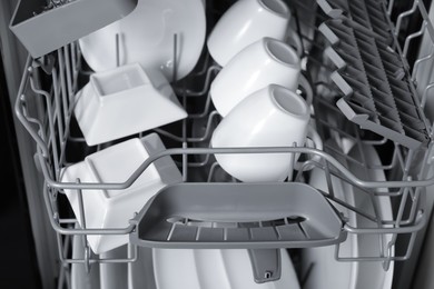 Open modern dishwasher with clean tableware, closeup