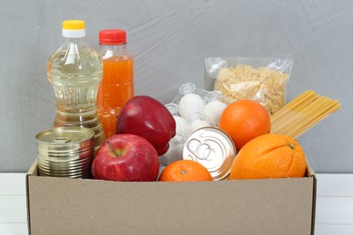 Humanitarian aid. Different food products for donation in box on white wooden table, closeup