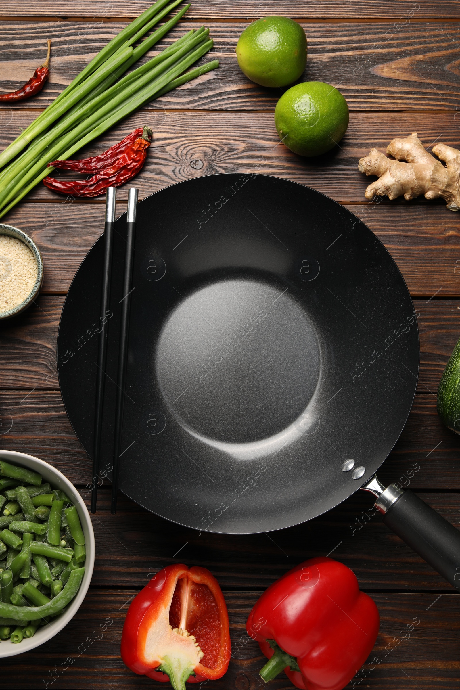 Photo of Black wok, chopsticks and products on wooden table, flat lay