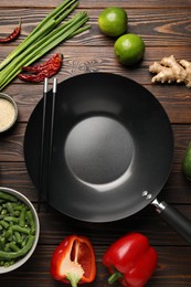 Black wok, chopsticks and products on wooden table, flat lay