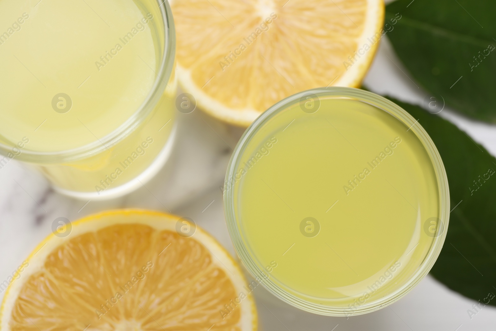 Photo of Tasty limoncello liqueur, half of lemon and green leaves on table, top view