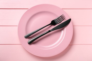 Ceramic plate with cutlery on pink wooden table, top view