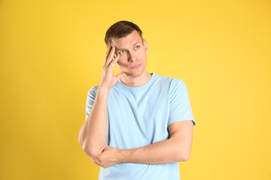 Thoughtful man in casual outfit on yellow background