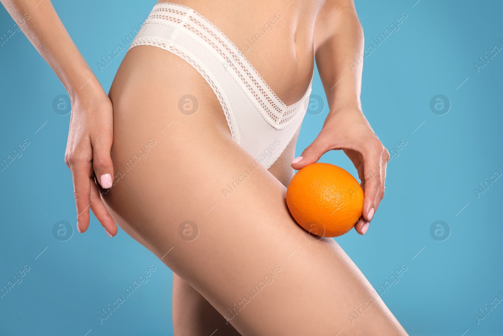 Photo of Closeup view of slim woman in underwear with orange on light blue background. Cellulite problem concept