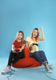 Young woman and teenage girl playing video games with controllers on color background. Space for text
