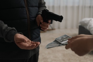 Woman giving money to criminal with gun indoors, closeup. Armed robbery