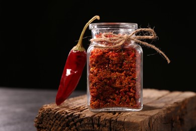 Chili pepper flakes in jar and pod on table against black background, space for text