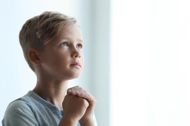 Little boy with hands clasped together for prayer on light background. Space for text