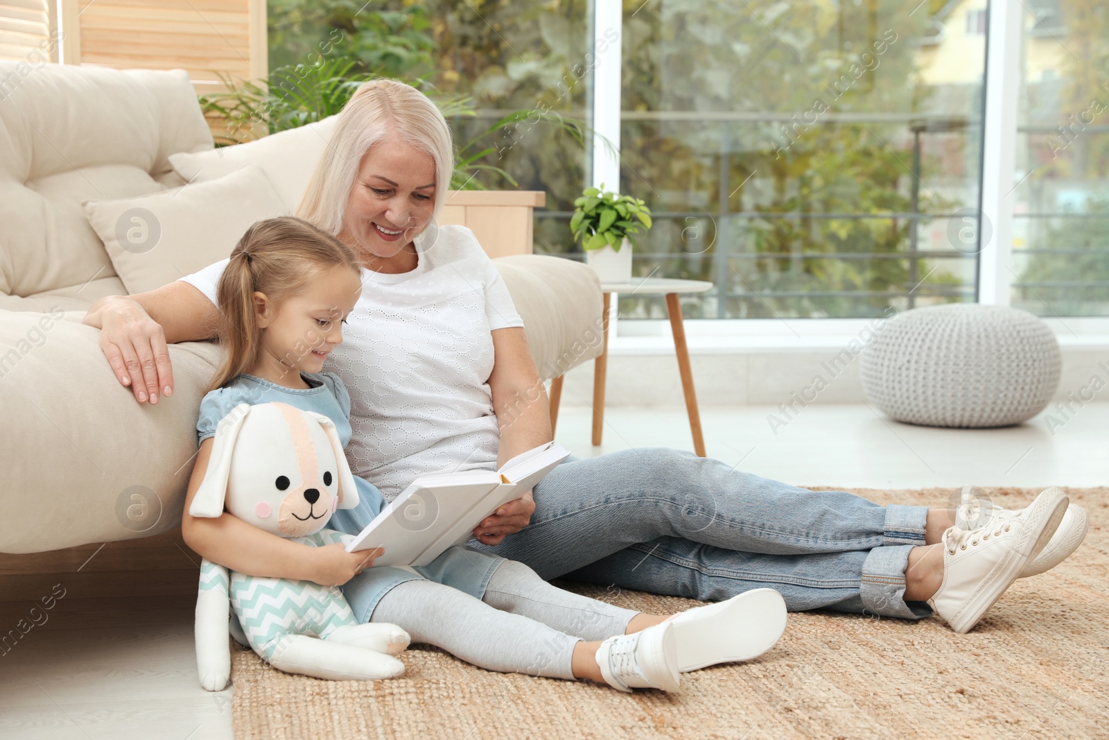 Photo of Happy grandmother with her granddaughter reading book together at home