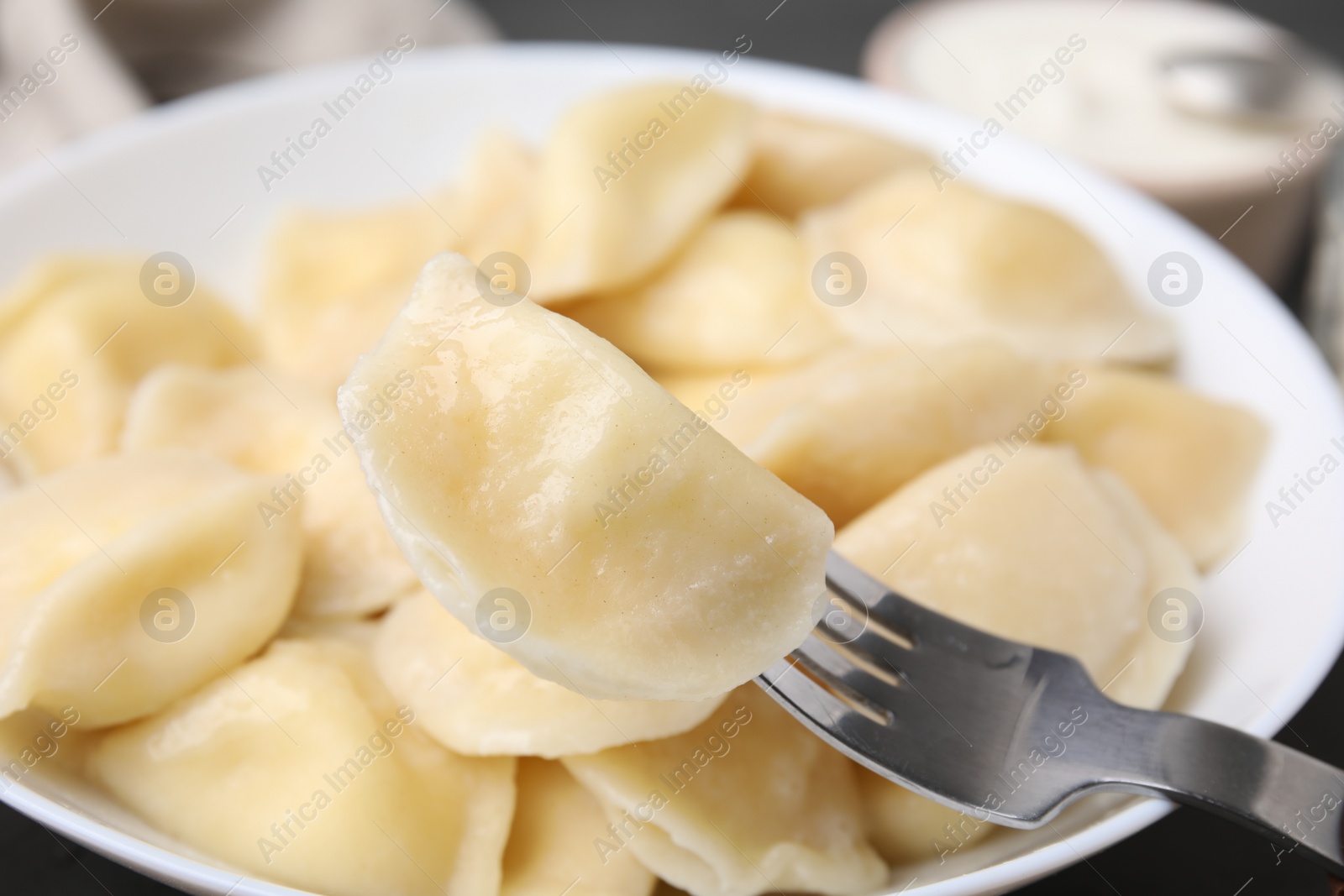 Photo of Delicious dumpling (varenyk) with cottage cheese on fork over bowl, closeup