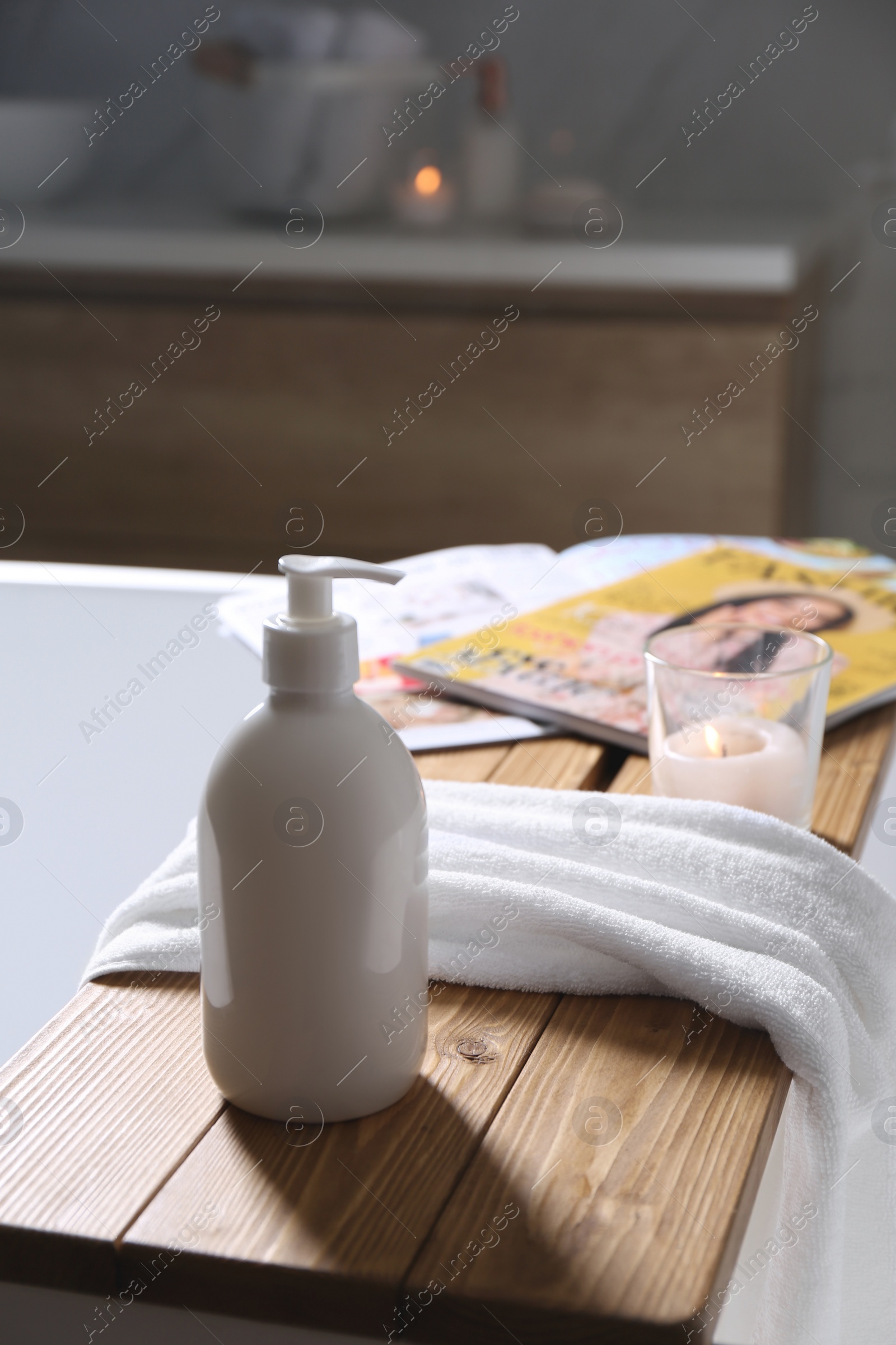 Photo of Wooden bath tray with shower gel, candle and fresh towel on tub indoors