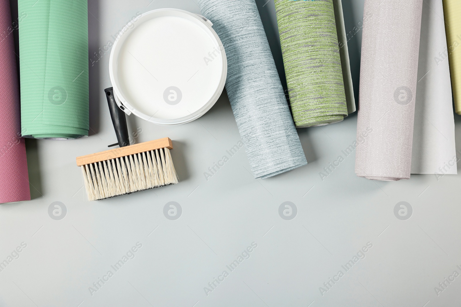 Image of Wallpaper rolls, brush and bucket of glue on light grey background, flat lay