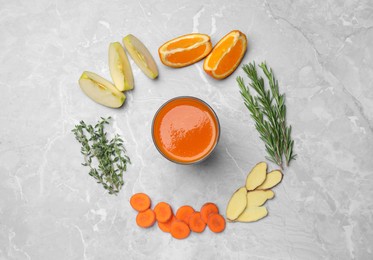Flat lay composition with healthy carrot juice in glass and ingredients on grey marble table