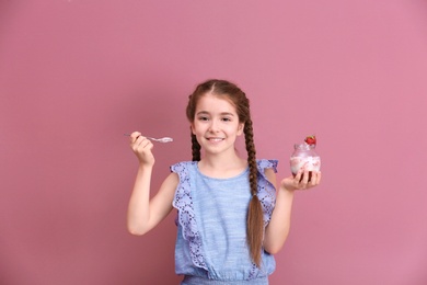 Cute girl eating tasty yogurt on color background