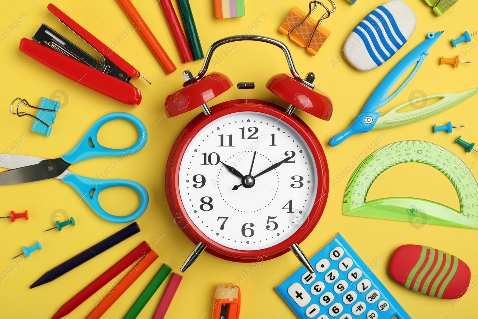 Photo of Flat lay composition with alarm clock and different stationery on yellow background. School time