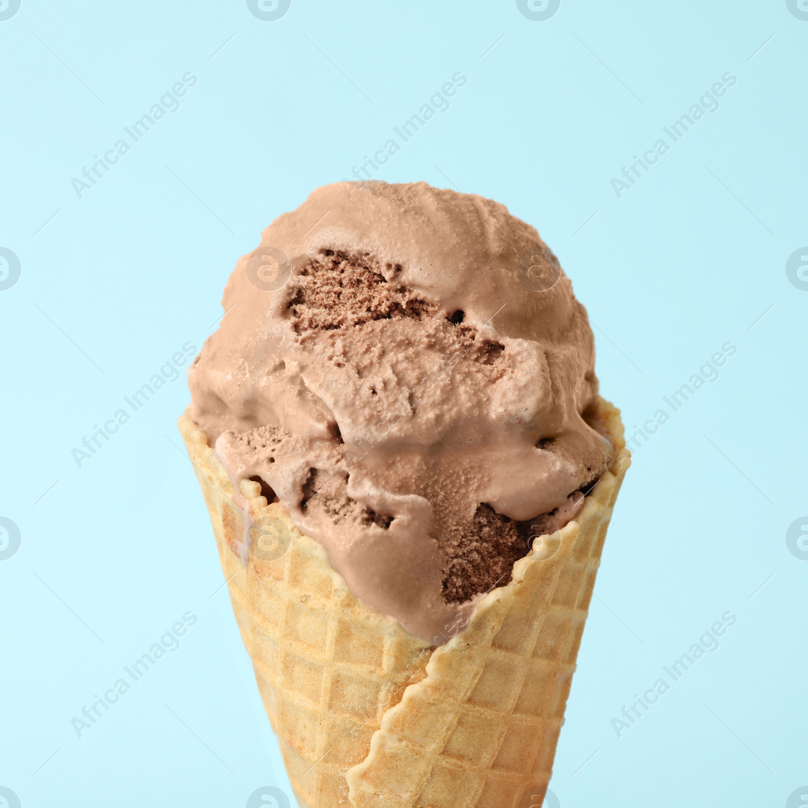 Photo of Delicious chocolate ice cream in waffle cone on light blue background, closeup