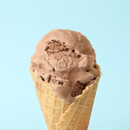 Delicious chocolate ice cream in waffle cone on light blue background, closeup