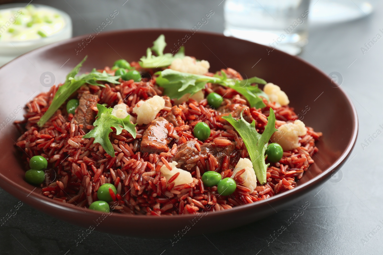 Photo of Tasty brown rice with meat and vegetables on dark grey table, closeup