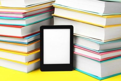 Photo of Modern e-book reader and stacks of hard cover books on yellow background, closeup