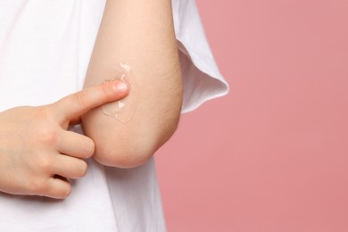 Child applying ointment onto elbow against pink background, closeup. Space for text