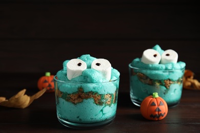 Photo of Delicious desserts decorated as monsters on wooden table. Halloween treat