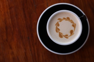 Ceramic cup of aromatic coffee with foam on wooden table, top view. Space for text