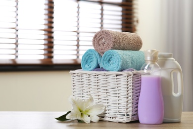 Photo of Clean towels in basket with lily and detergents on table indoors. Space for text