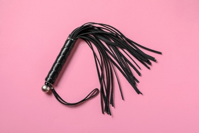 Photo of Black whip on pink background, top view. Sexual role play accessory