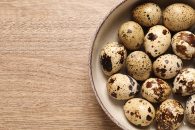 Photo of Bowl with quail eggs on wooden table, top view. Space for text
