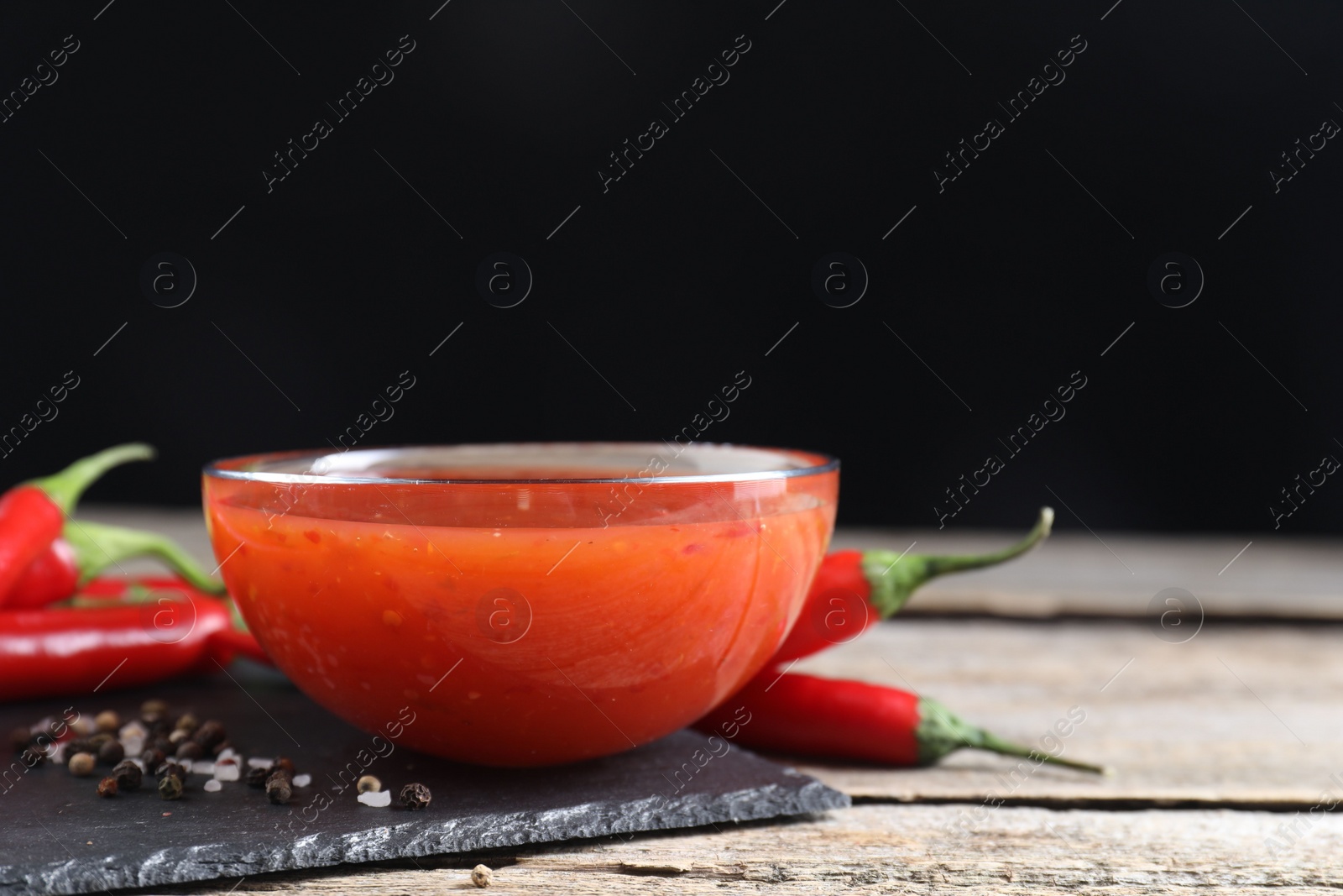 Photo of Spicy chili sauce in bowl on wooden table. Space for text