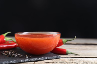 Photo of Spicy chili sauce in bowl on wooden table. Space for text