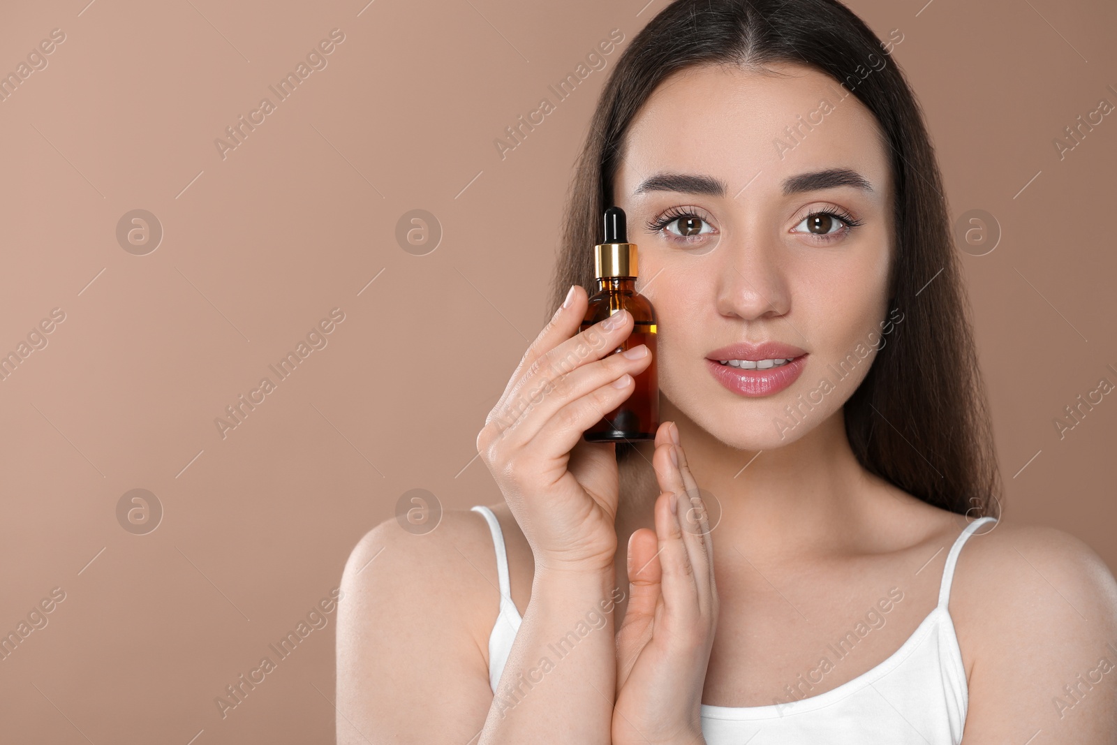 Photo of Beautiful young woman with essential oil on brown background. Space for text