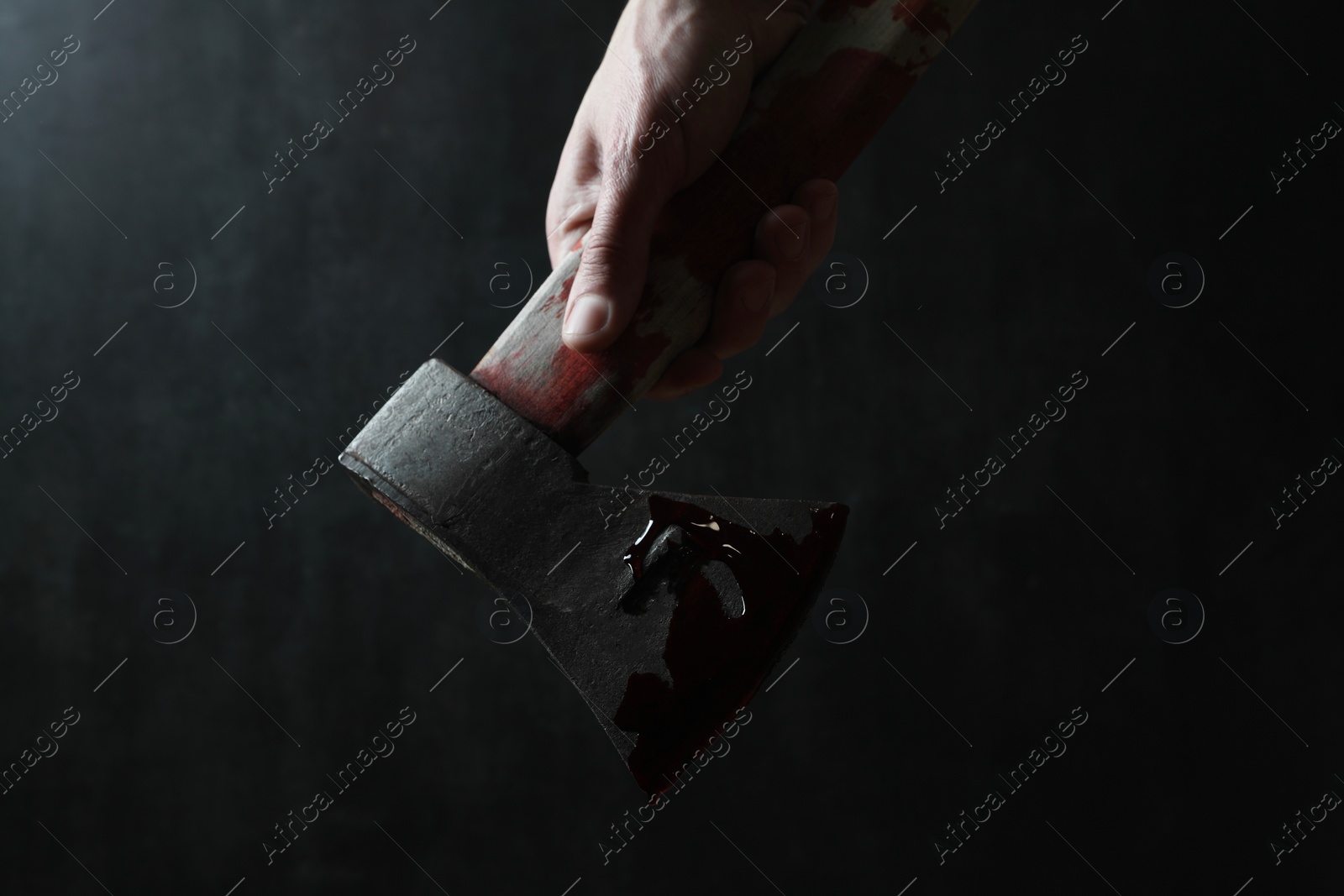 Photo of Man holding bloody axe on dark gray background, closeup