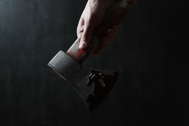 Man holding bloody axe on dark gray background, closeup